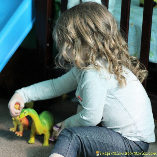 girl playing with two dinosaur toys