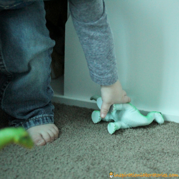 toddler picking up toy dinosaur from floor