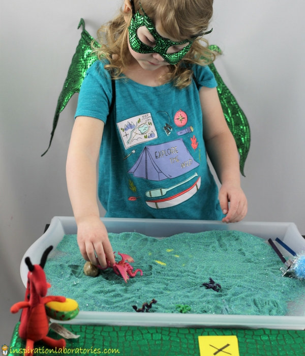 preschool girl drawing lines in a sand tray with a toy dragon