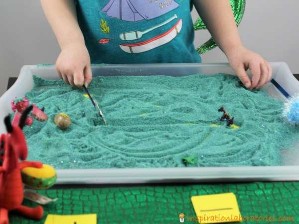 preschool girl drawing lines in a sand tray with a magic wand