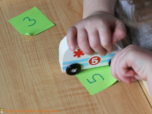 preschooler playing a matching game with the number 5 and a toy ambulance