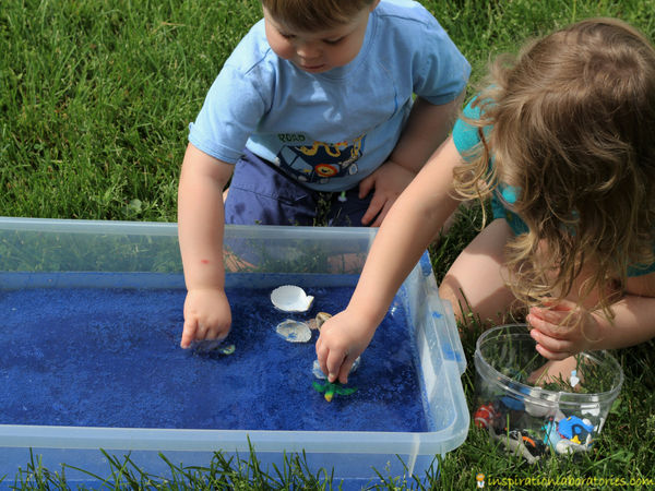 children playing in an ocean themed sensory bin with blue sand, water, sea shells, and ocean animal toys