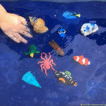 Set up a simple ocean sensory bin with colored sand and water.