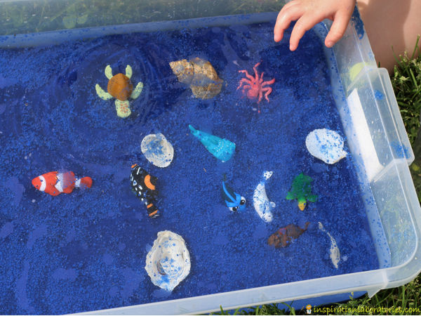 ocean themed sensory bin with blue sand, water, sea shells, and ocean animal toys
