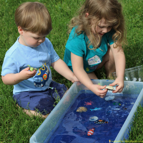 children playing in an ocean themed sensory bin with blue sand, water, sea shells, and ocean animal toys