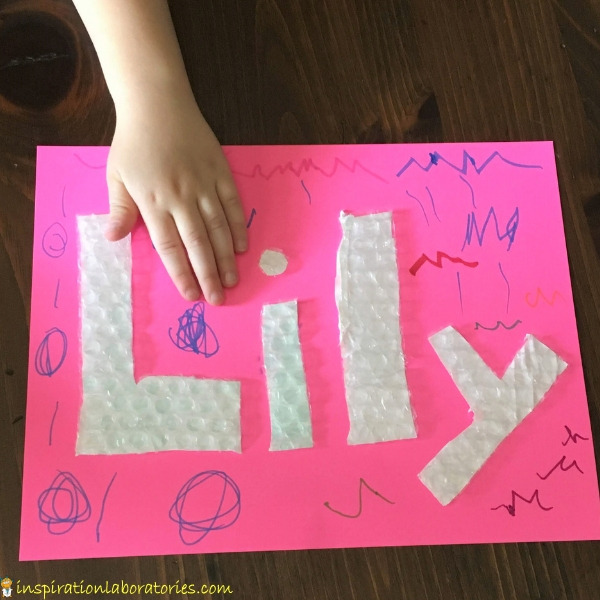 child's hand touching bubble wrap letters