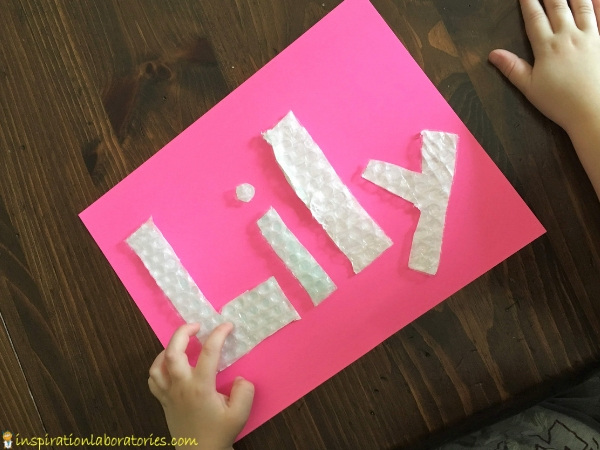 child's hand touching bubble wrap letters