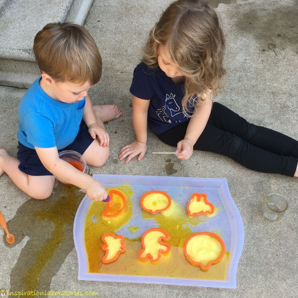 kids dropper colored vinegar onto baking soda in Halloween themed cookie cutters
