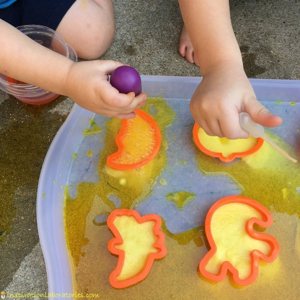 kids dropper colored vinegar onto baking soda in Halloween themed cookie cutters