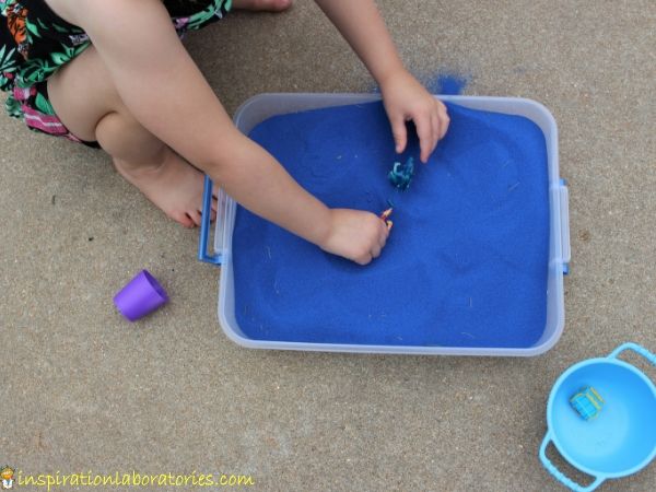 Sensory bins are great for pretend play. Blue colored sand with toy dragons shown.