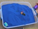 Sensory bins are great for pretend play. Blue colored sand with toy dragons shown.