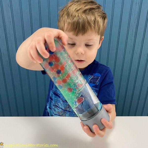 child holding a sensory bottle filled with oil and water beads